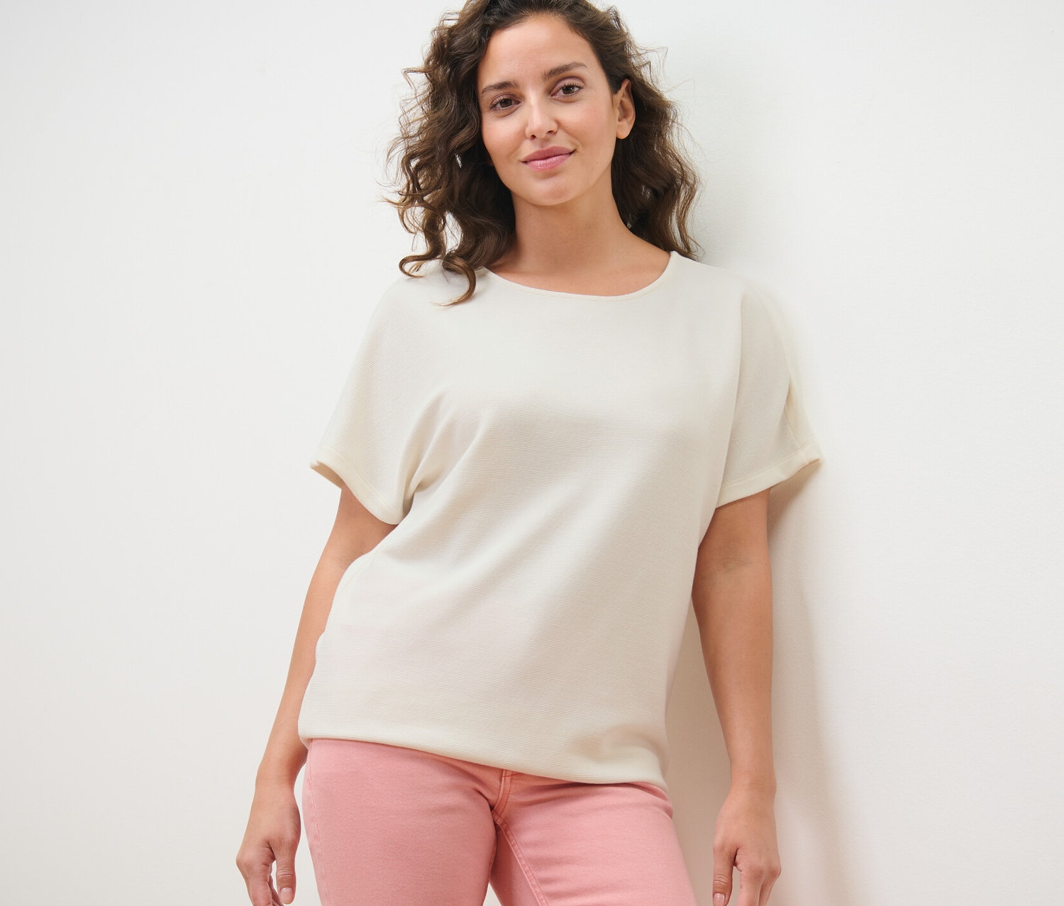 Kadın krem rengi bluzu ve pembe pantolonuyla poz veriyor.