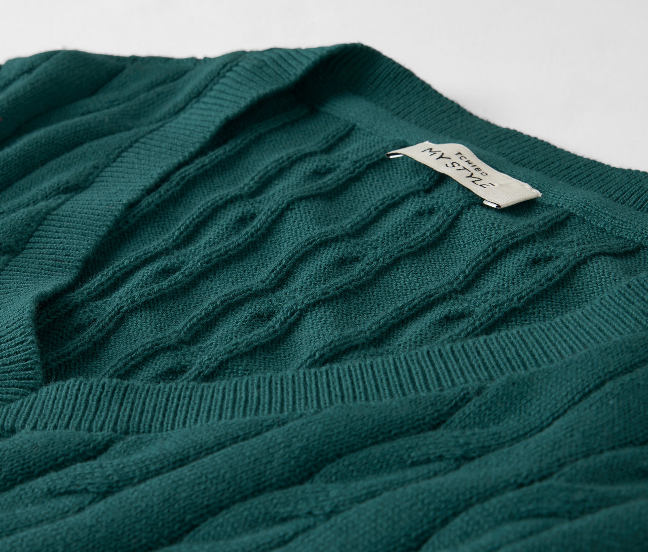 Zümrüt yeşili, V yakalı, örgü desenli bir kazağın yakın çekim fotoğrafı, üzerinde etiketi bulunuyor.