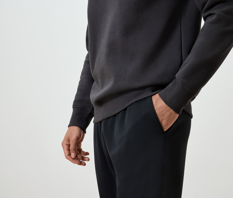 Adamın eli siyah eşofmanının cebinde ve koyu gri bir sweatshirt giyiyor.