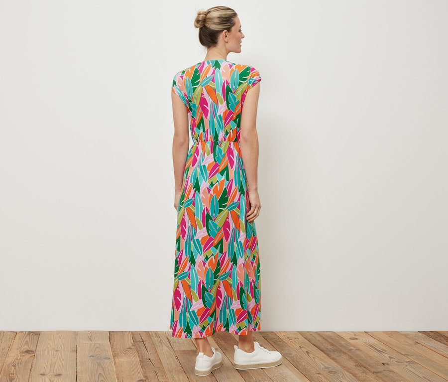 Bir kadın kameraya arkası dönük duruyor, üzerinde düğümlü jarse elbise ve beyaz spor ayakkabılar var.