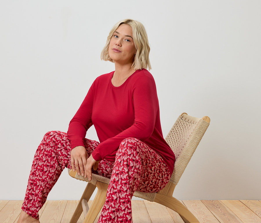 Sarışın bir kadın hasır bir sandalyede oturuyor ve kırmızı bir pijama giyiyor.