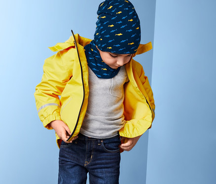 Sarı ceketli çocuk fermuarını kapatıyor, desenli bere ve boyunluk takıyor.