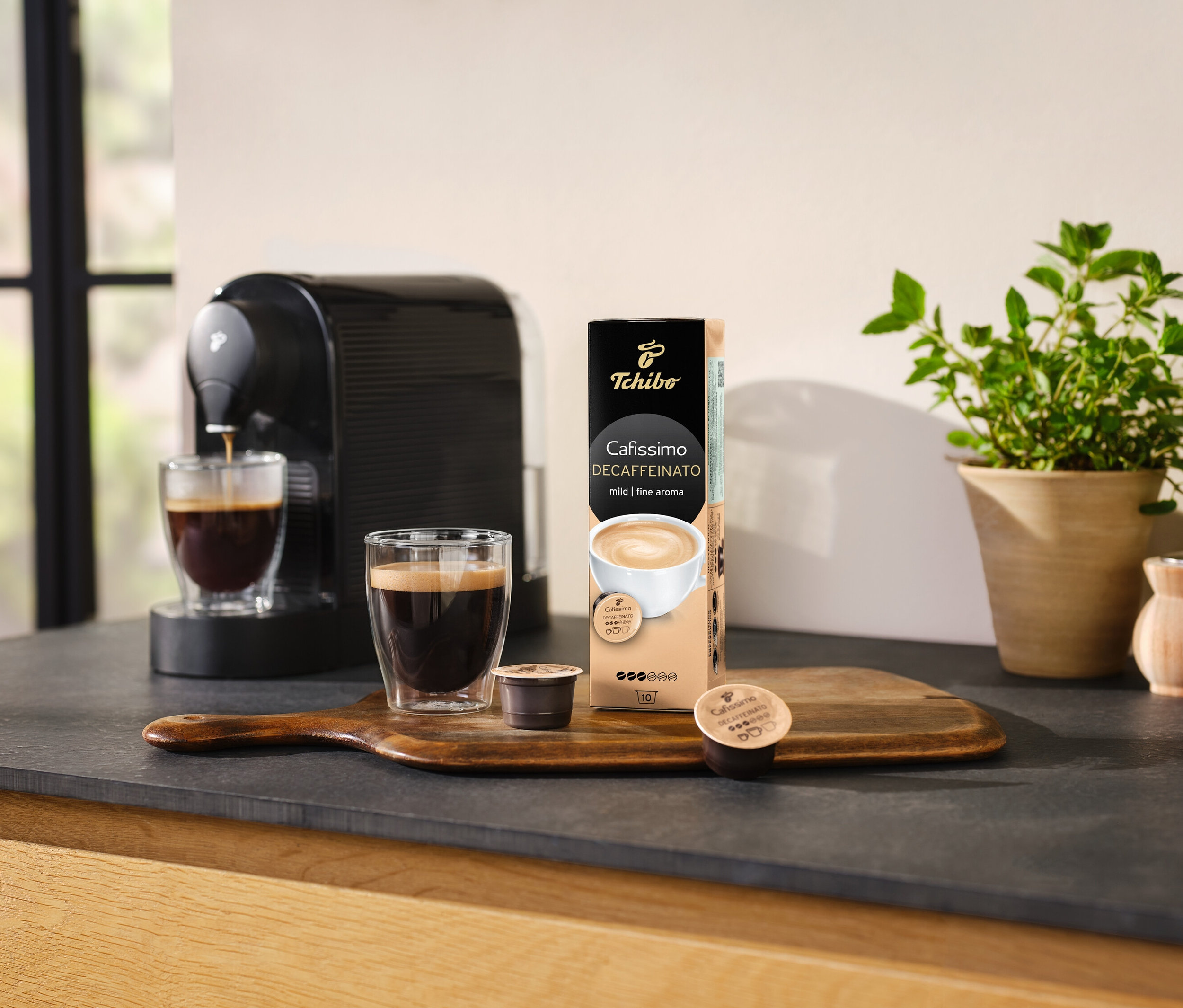 Kahve makinesi, bir bardak kahveyi Cafissimo Decaffeinato kapsül paketinin yanına döküyor.