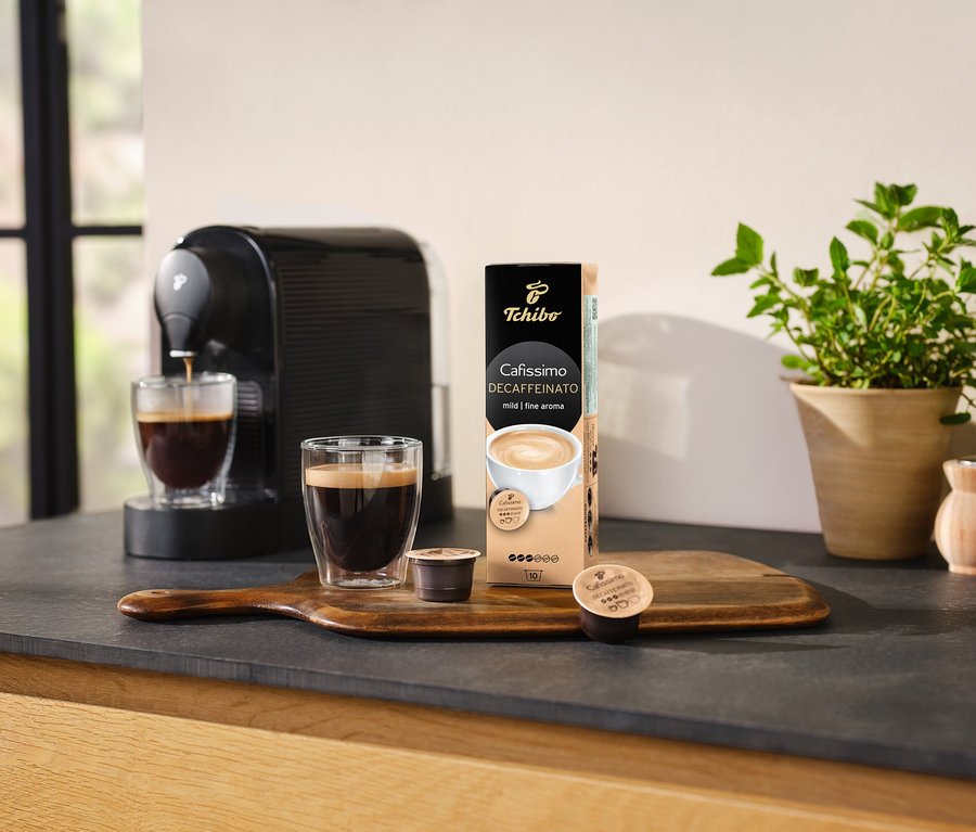 Kahve makinesi, bir bardak kahveyi Cafissimo Decaffeinato kapsül paketinin yanına döküyor.