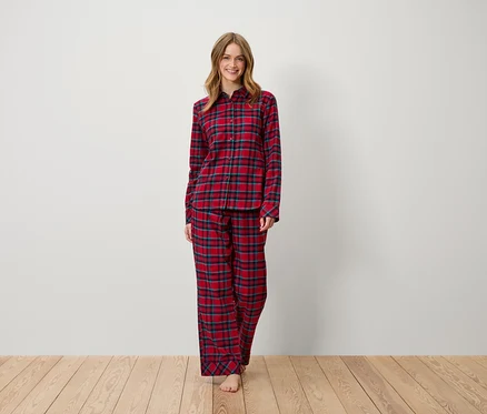 Kadın ayakta duruyor ve gülümsüyor, kırmızı ekose pijama giymiş. 