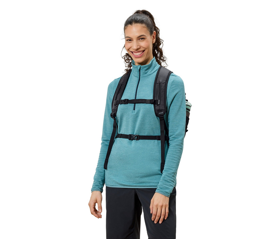 Siyah sırt çantası, mavi üst ve siyah pantolon giyen, gülümseyen kadın.