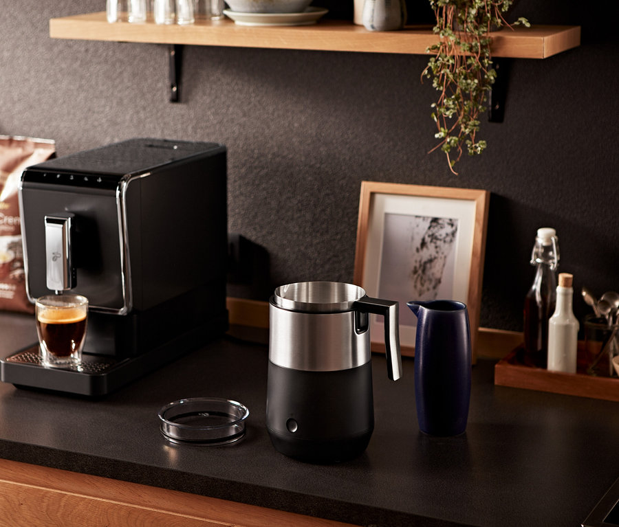 Espresso makinesi, siyah indüksiyonlu süt köpürtücünün yanındaki bardağa kahve döküyor.