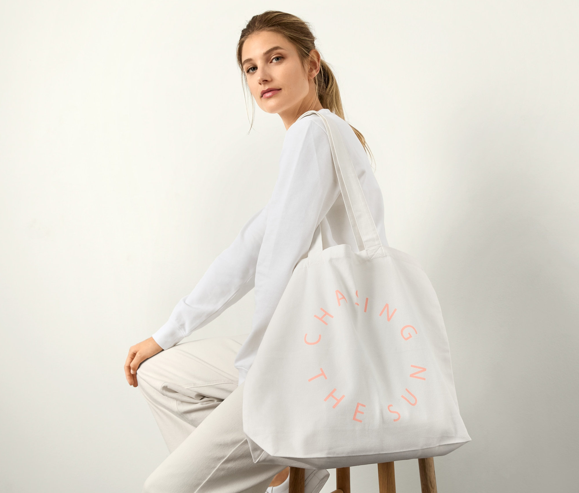 Kadın bir taburede oturuyor, omzunda organik pamuklu kanvas alışveriş çantası var.