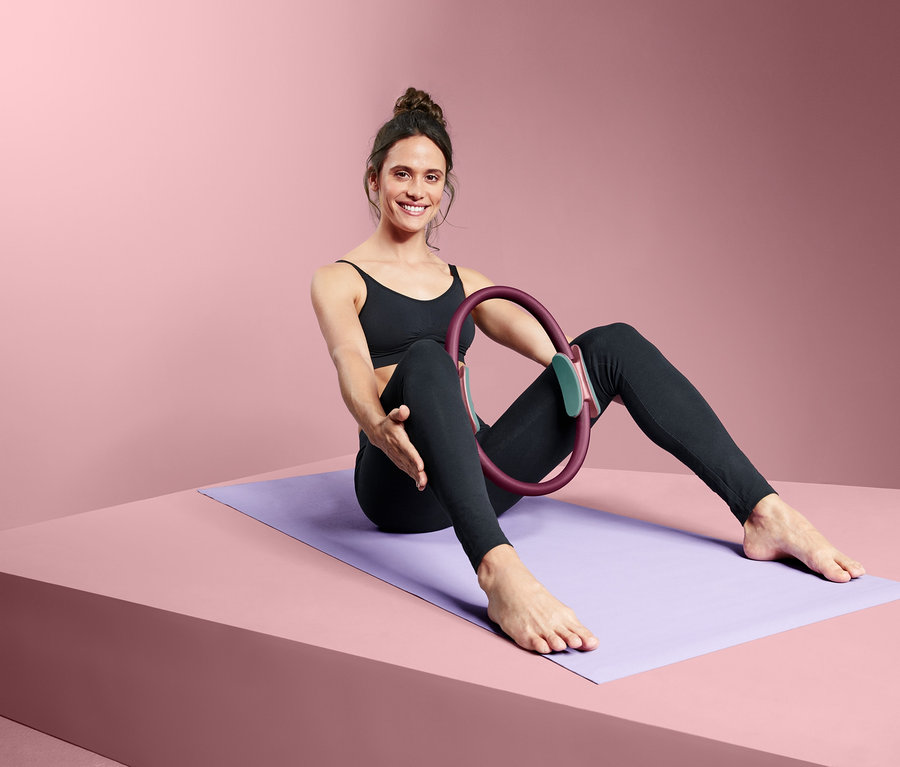 Kadın yoga matında oturuyor ve bir Pilates Halkası tutuyor.