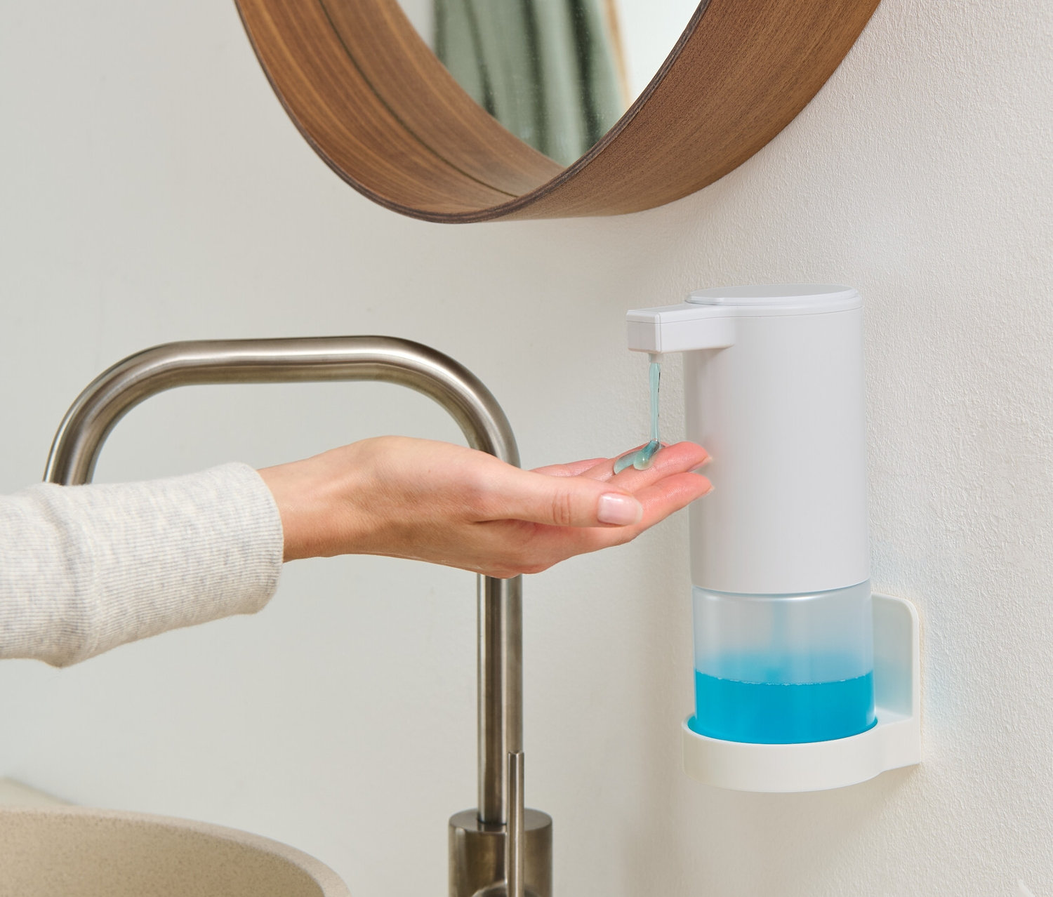 Kadın, duvara monte edilmiş sensörlü beyaz sabunluktan eline sabun alıyor.