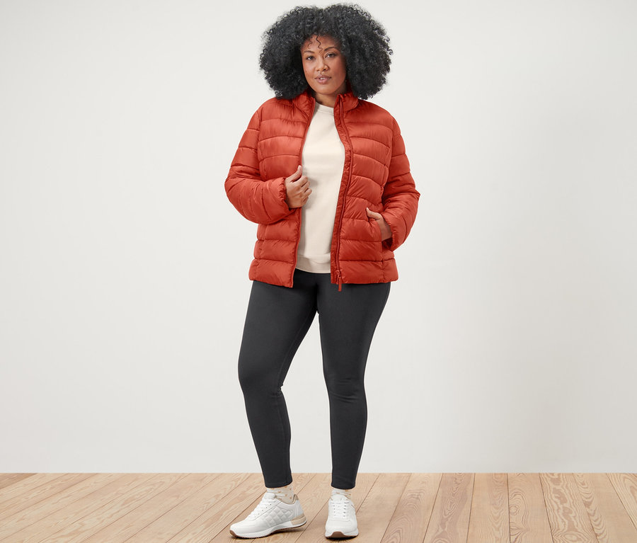 Kadın turuncu kapitone mont, nakışlı sweatshirt ve jegging ile poz veriyor.