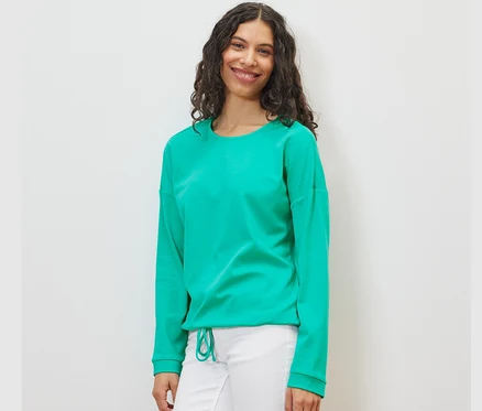 Kadın aqua rengi bir sweatshirt ve beyaz pantolon giyiyor.