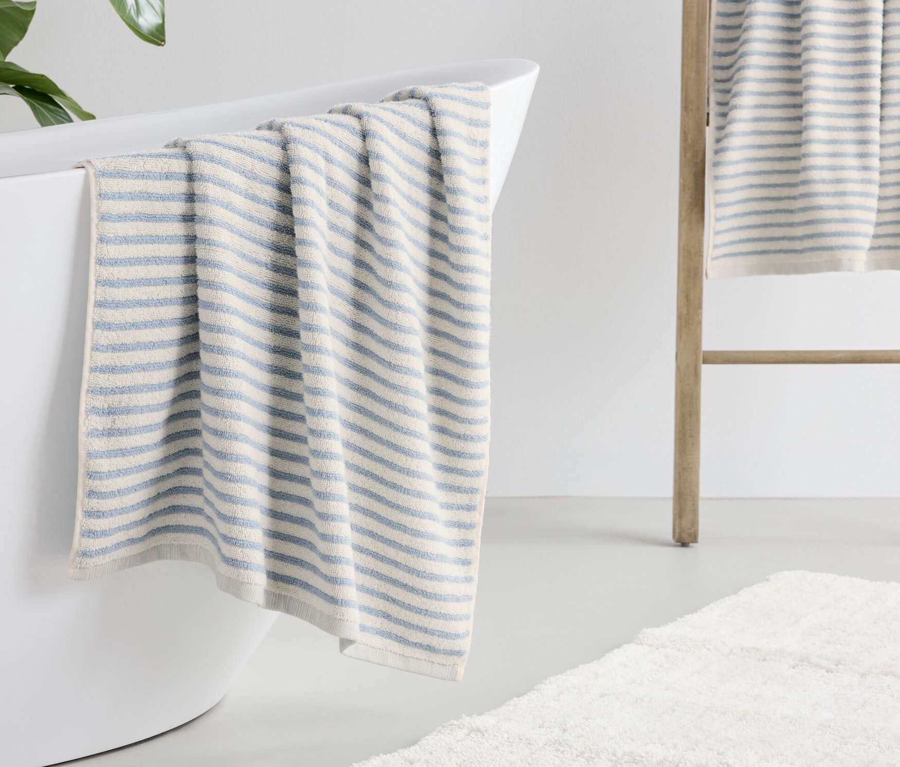 Mavi çizgili banyo havlusu beyaz bir küvetin kenarında duruyor.