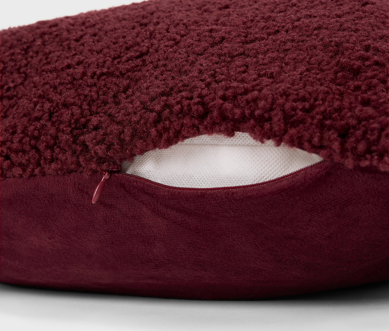 Fermuarlı bordo tüylü bir yastığın detayı.