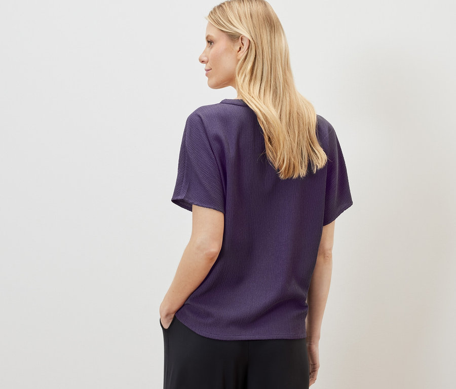 Sarışın bir kadın, dokulu kısa kollu bir bluz ve siyah pantolon giyiyor.