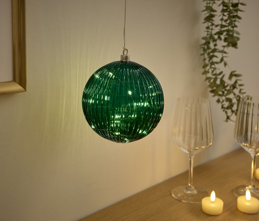 Yeşil cam küre, bardak ve mumların olduğu masanın üzerinde asılı duruyor.