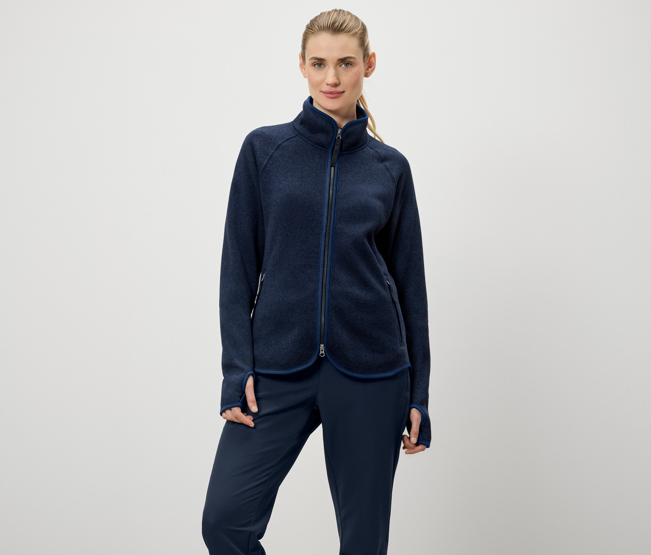 Kadın, lacivert fermuarlı bir polar ceket ve lacivert pantolon giyiyor.