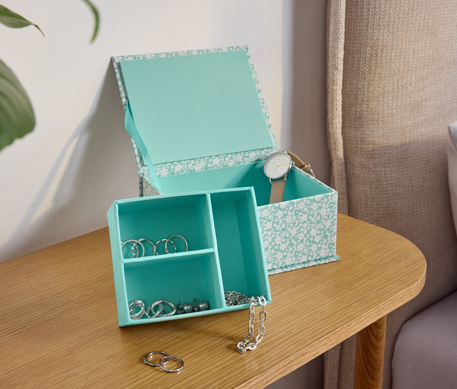 Ahşap bir komodinin üzerinde çiçek desenli turkuaz bir mücevher kutusu.