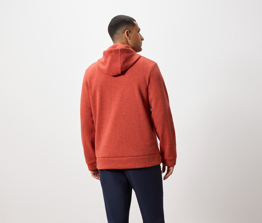 Sırtı kameraya dönük bir adam turuncu kapüşonlu bir sweatshirt ve lacivert pantolon giyiyor.