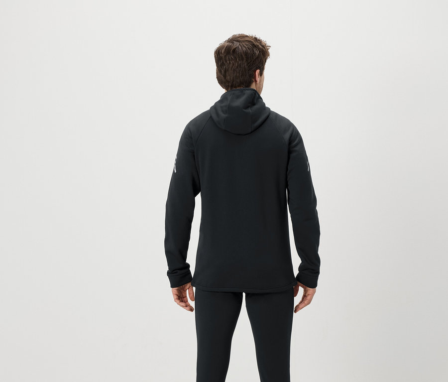Sırtı kameraya dönük bir adam siyah kapüşonlu bir sweatshirt ve siyah pantolon giyiyor.