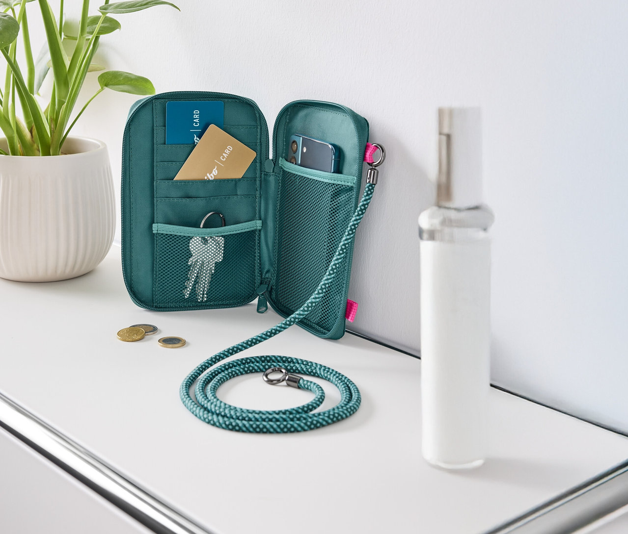 Açık, yeşil bir cüzdan beyaz bir masanın üzerinde duruyor, içinde kartlar, anahtarlar ve bir cep telefonu var.