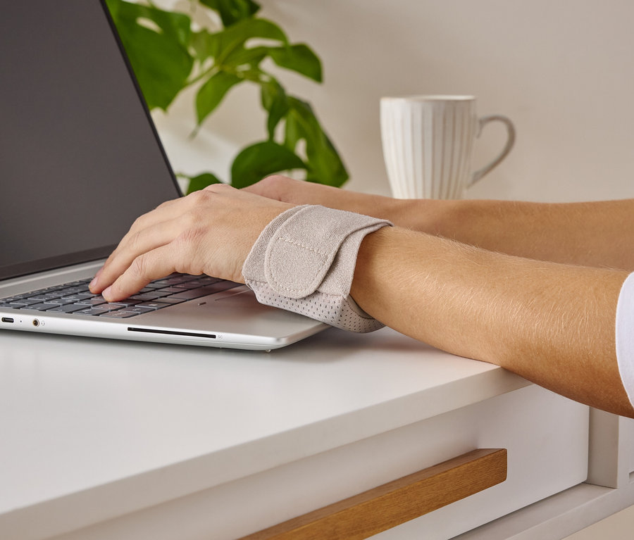 Kişi dizüstü bilgisayarda yazı yazıyor ve bilek desteği takıyor.