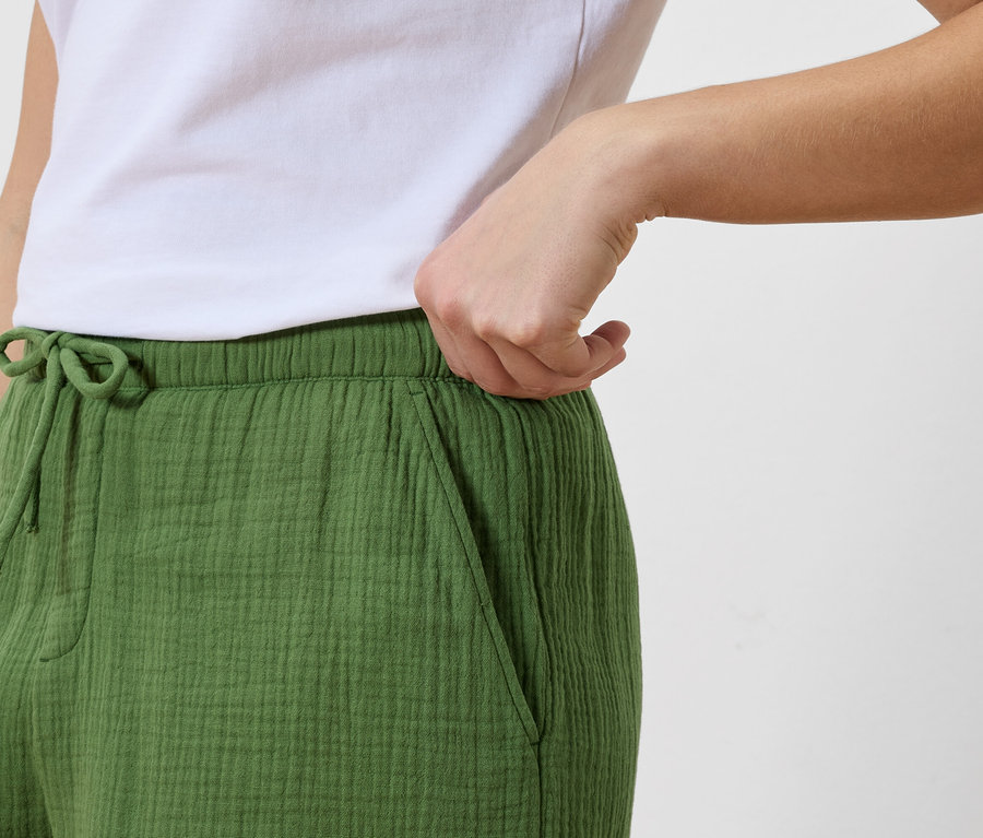 Kadın, beyaz tişörtüyle birlikte bağcıklı yeşil bir pantolonun cebine uzanıyor.