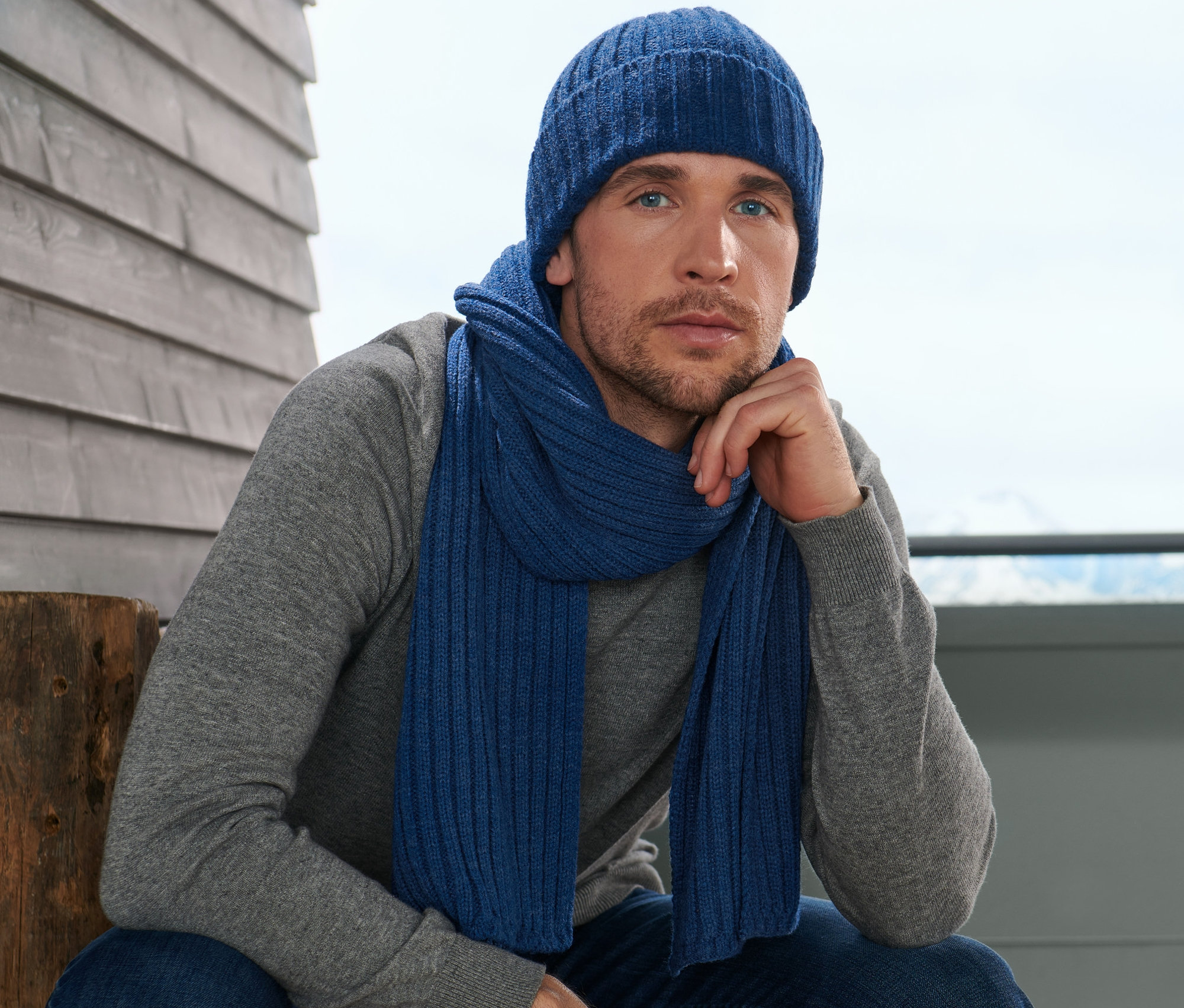 Adam örgü atkı ve bere takmış oturuyor.