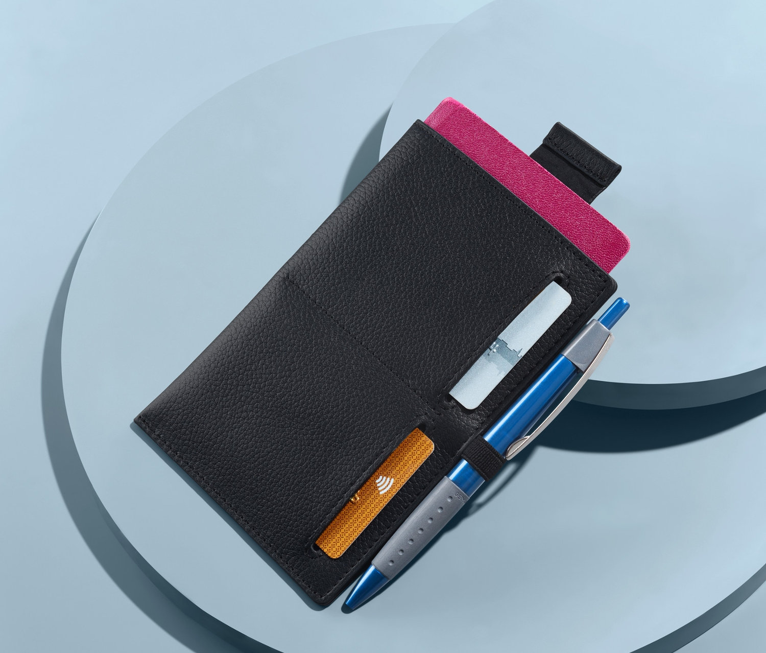 Mavi arka planda pasaport, kartlar ve kalem ile birlikte siyah deri pasaport cüzdanı.