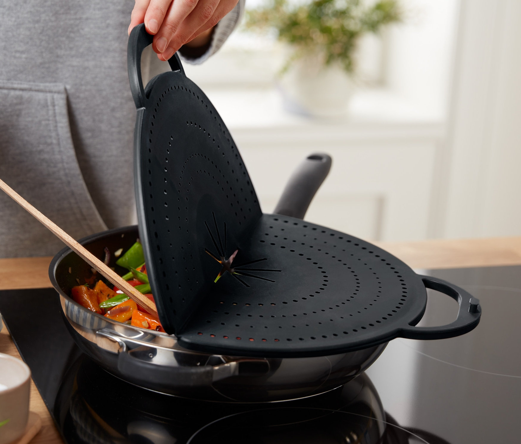 Bir kişi sebzeli bir tavanın üzerinde 4'ü 1 Arada Yağ Sıçratmaz tutuyor.