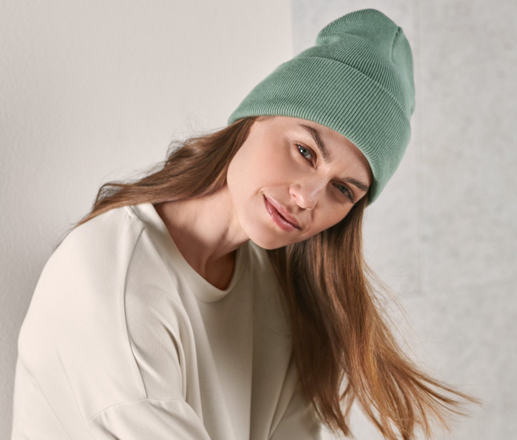 Kahverengi saçlı bir kadın açık yeşil organik pamuklu örgü bere takıyor.