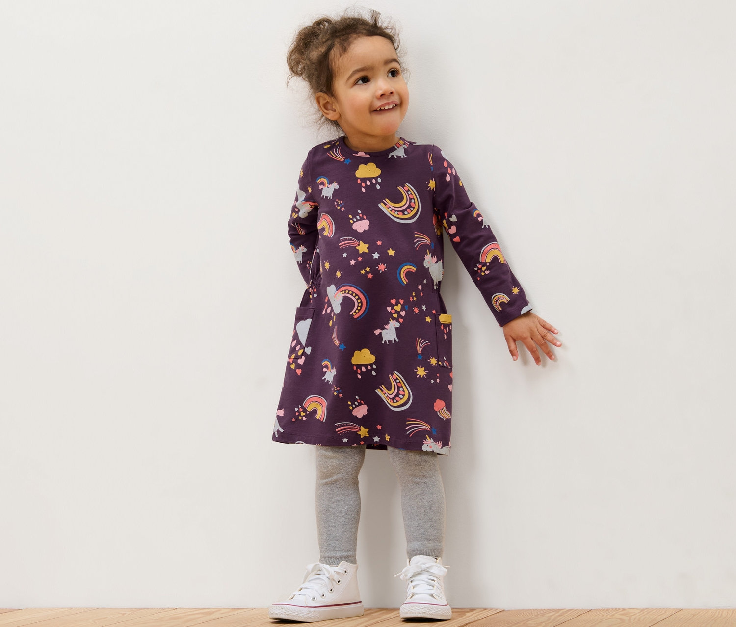 Gökkuşağı, yıldız ve unicorn desenli çocuk Jersey elbisesi giyen gülümseyen kız çocuğu.