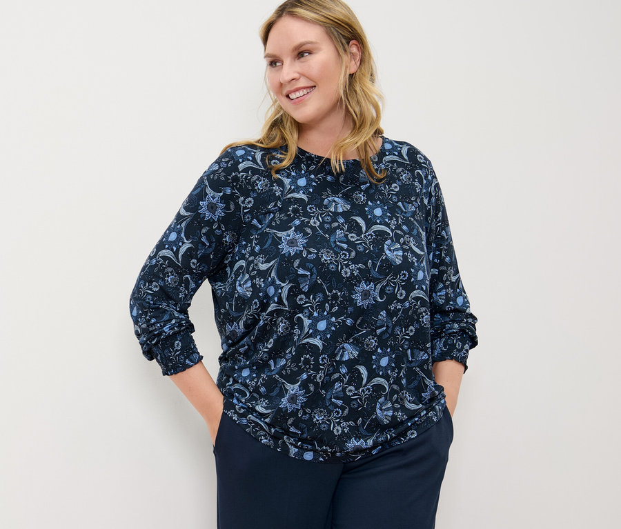 Kadın, baskılı bluz ve konforlu jersey pantolon ile poz veriyor.