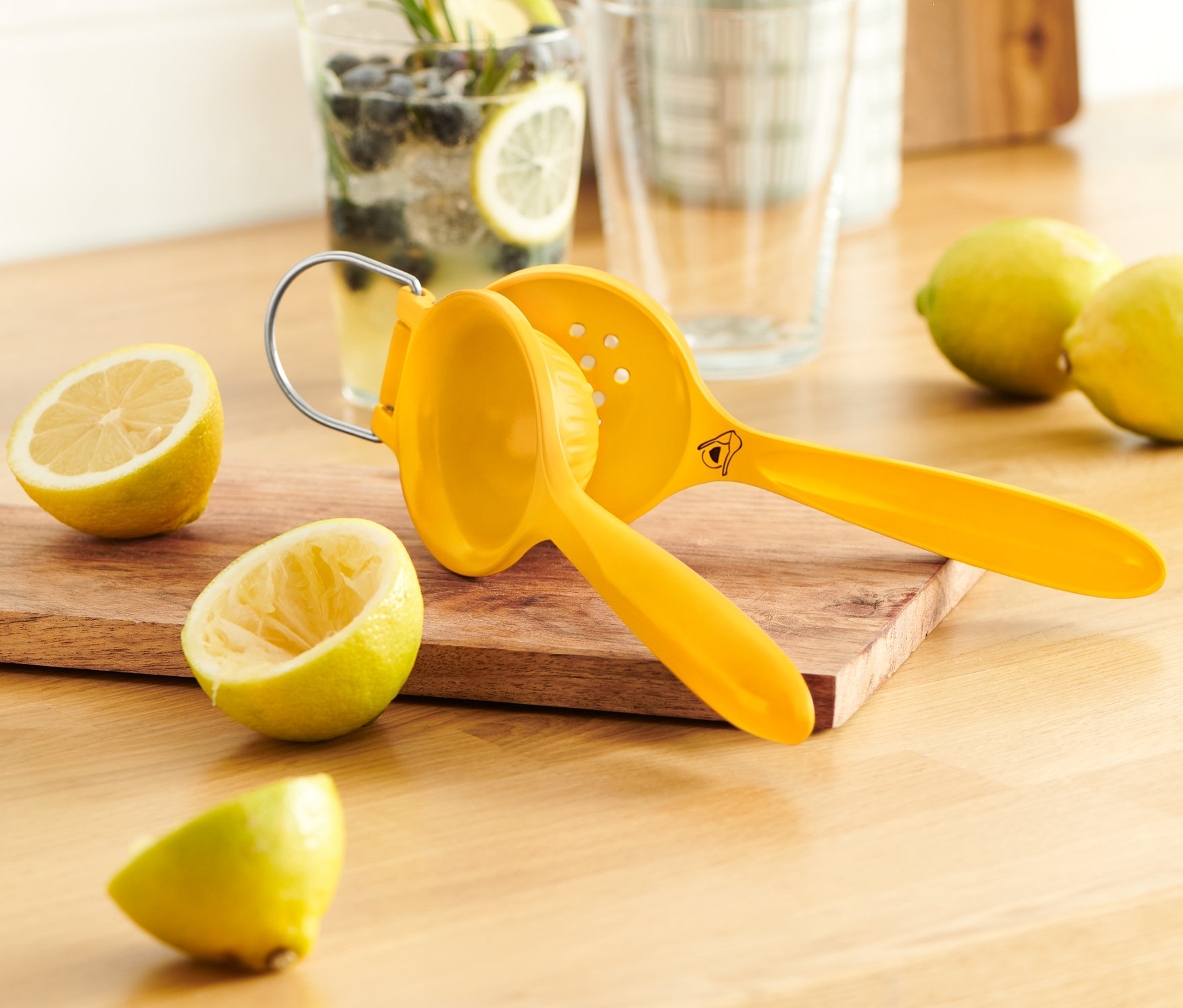 Limonların ve limonlu su bardağının yanında, ahşap bir tahta üzerinde sarı bir limon sıkacağı.