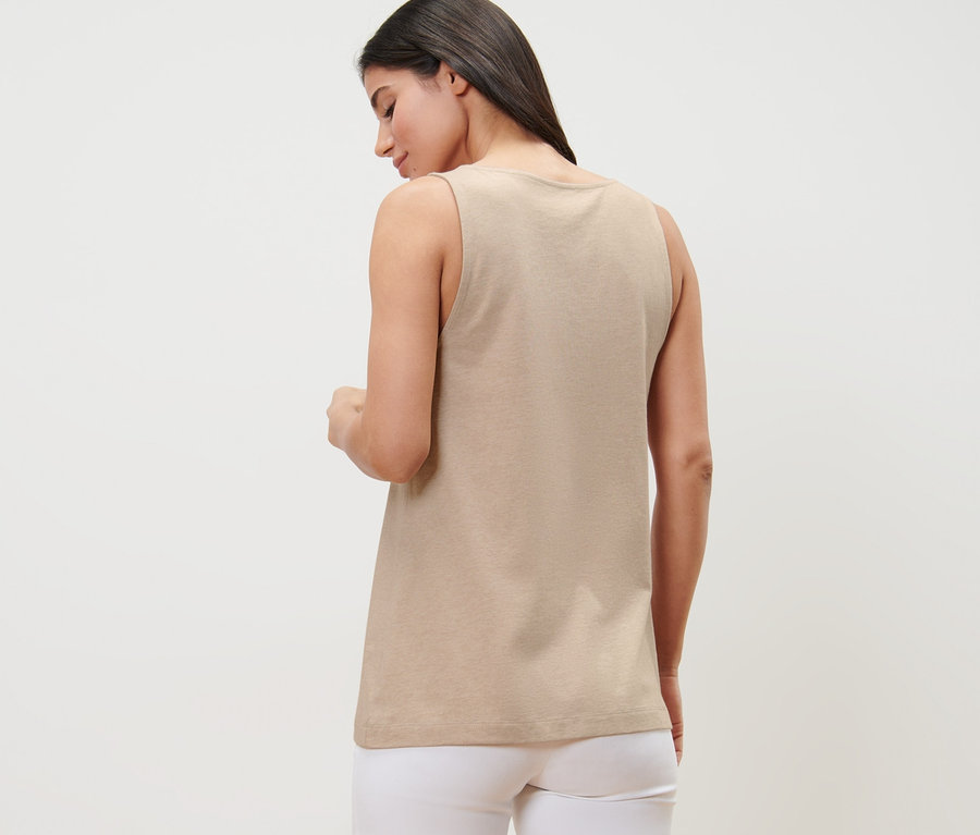 Arkası dönük bir kadın, düğme şeritli kırçıllı bej bir üst ve beyaz pantolon giyiyor.