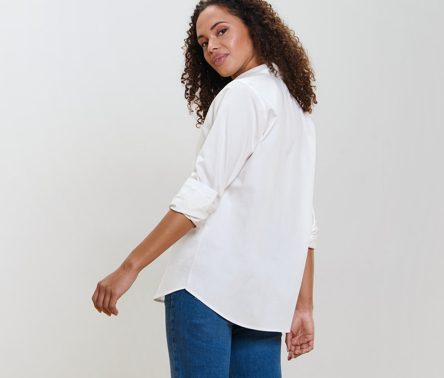 Kadın omzunun üzerinden bakıyor ve beyaz bir bluz giyiyor.