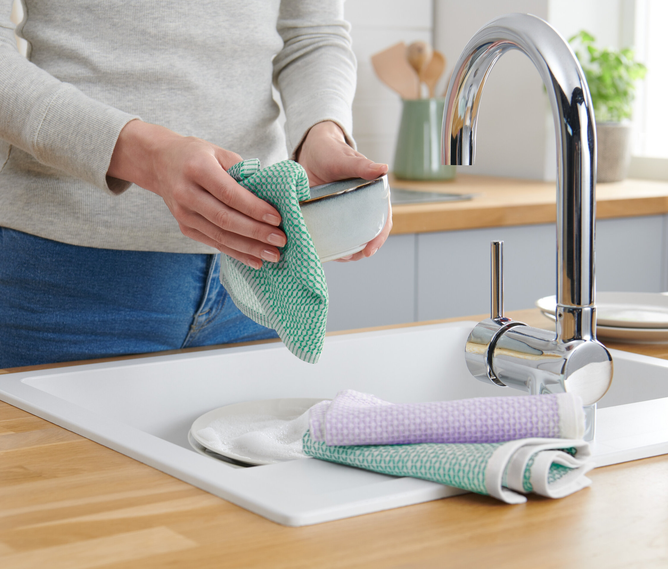 Kadın, musluk ve sabunluk bulunan lavaboda yeşil bir bulaşık beziyle bir kaseyi kuruluyor.