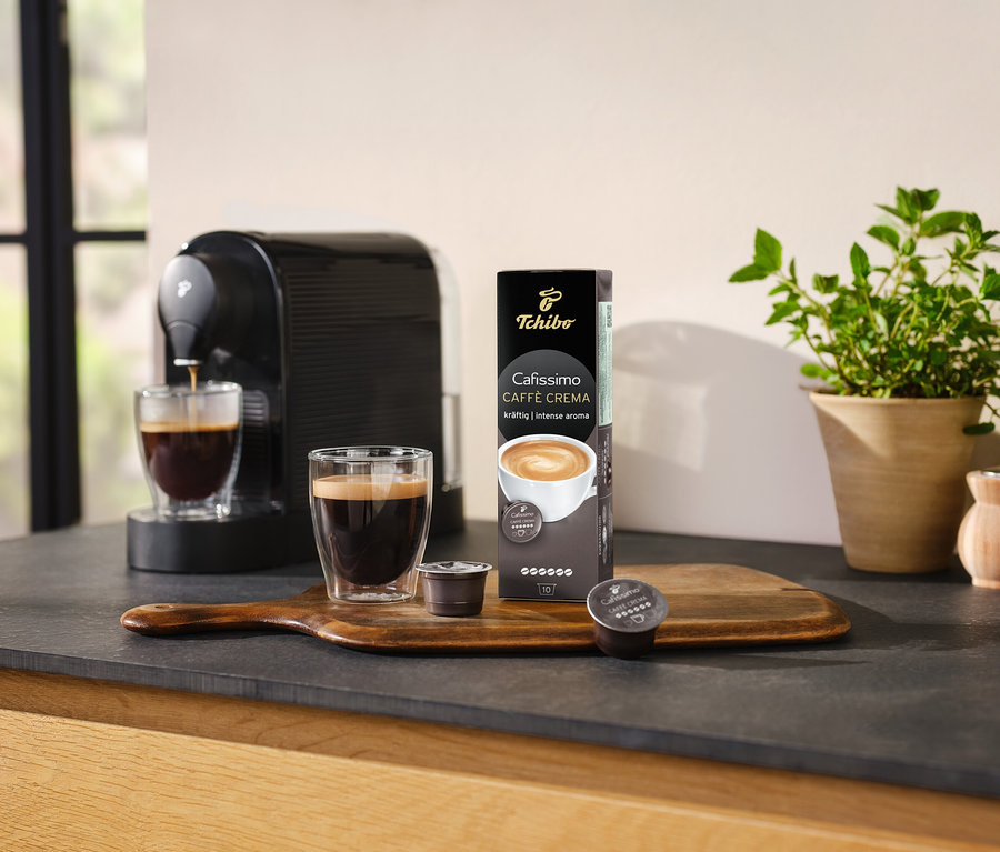 Kahve makinesi, bir bardak kahveyi Cafissimo Caffè Crema – 10 kapsül paketinin yanına hazırlıyor.