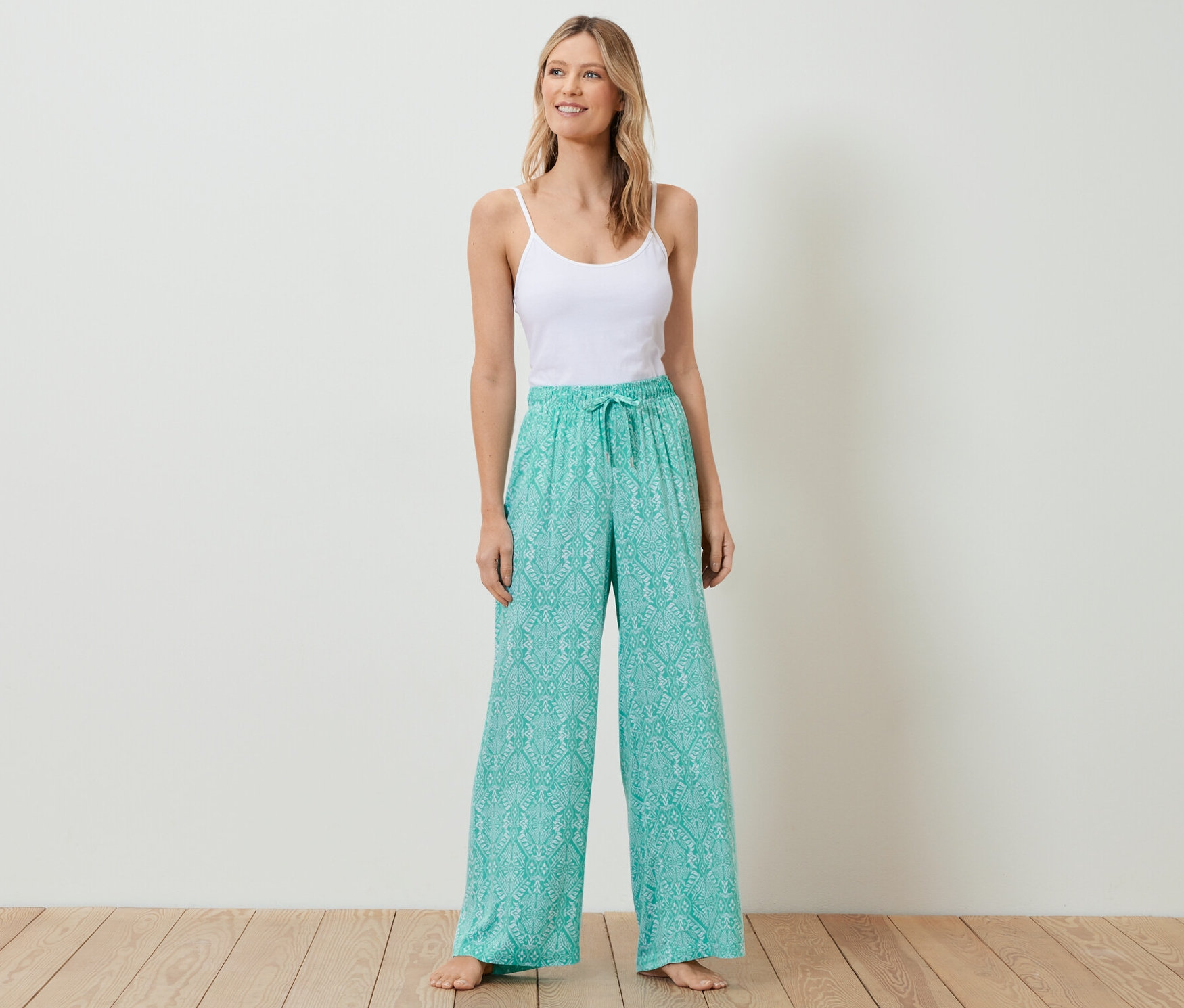 Bir kadın ayakta duruyor, beyaz bir bluz ve rahat bir pantolon giyiyor.