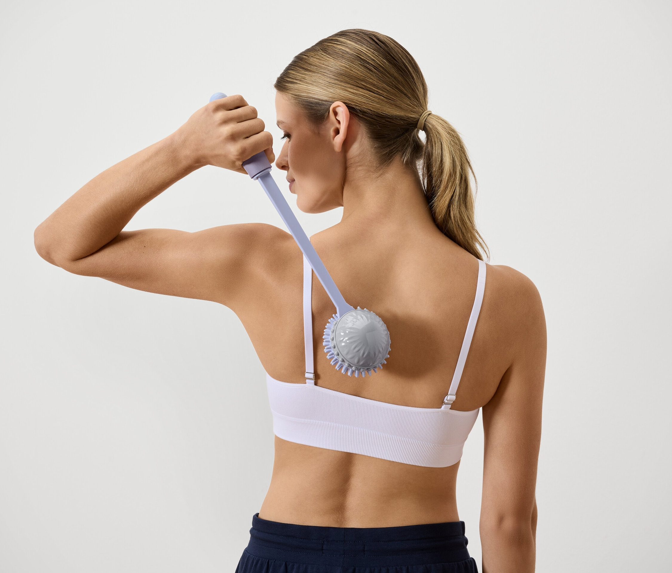 Sırtı görünen bir kadın uzun saplı bir masaj aletiyle sırtına masaj yapıyor.