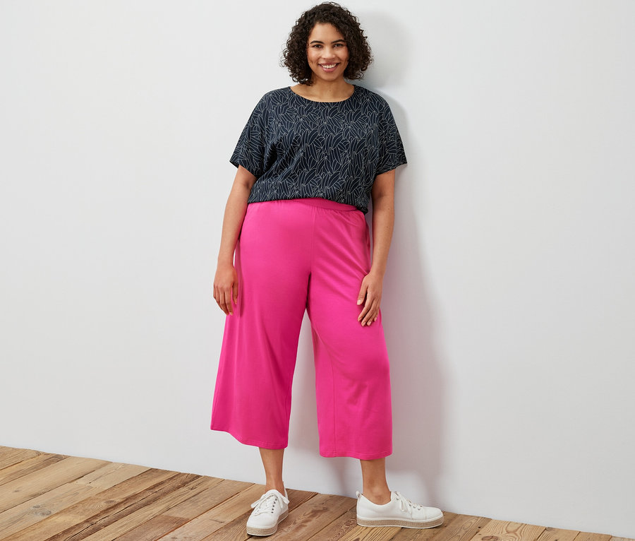 Bir kadın ayakta duruyor, üzerinde lacivert, kısa kollu düşük omuzlu tişört ve pembe Jersey Culotte Pantolon var.