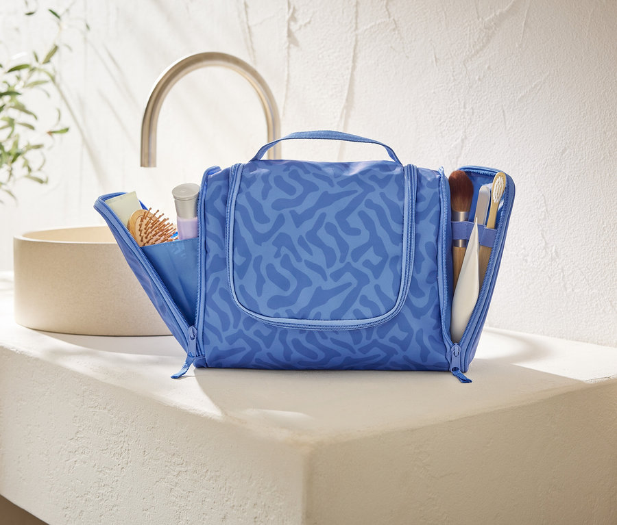 Açık, mavi, soyut desenli bir makyaj çantası, banyoda beyaz bir tezgahın üzerinde duruyor.