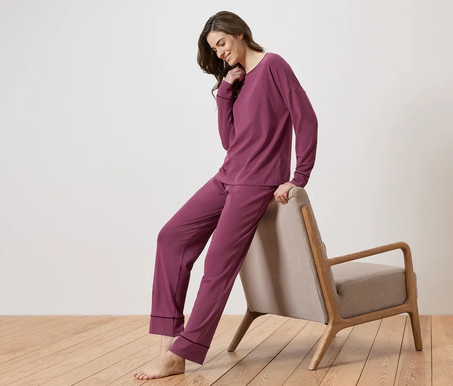Bordo renkli pijama takımı giyen bir kadın sandalyeye yaslanıyor.