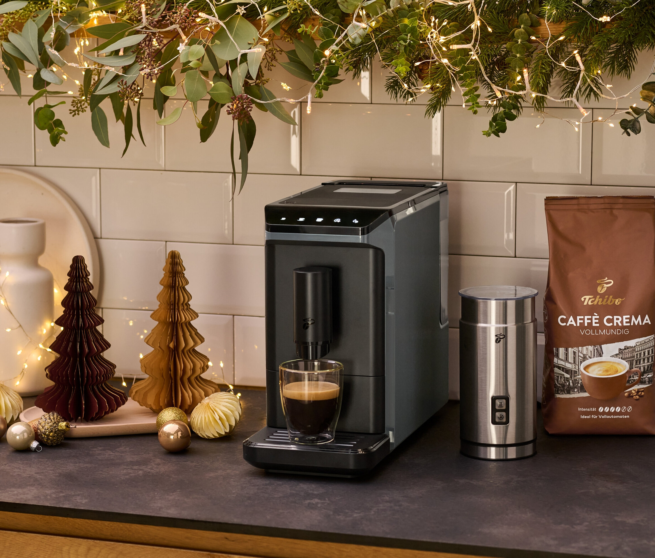 Gri renkli »Esperto mini« kahve makinesi, bir mutfak tezgahında süt köpürtücü ve bir paket kahvenin yanında duruyor.