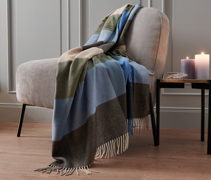 Bej bir koltuğun üzerinde çizgili bir ekose battaniye var.