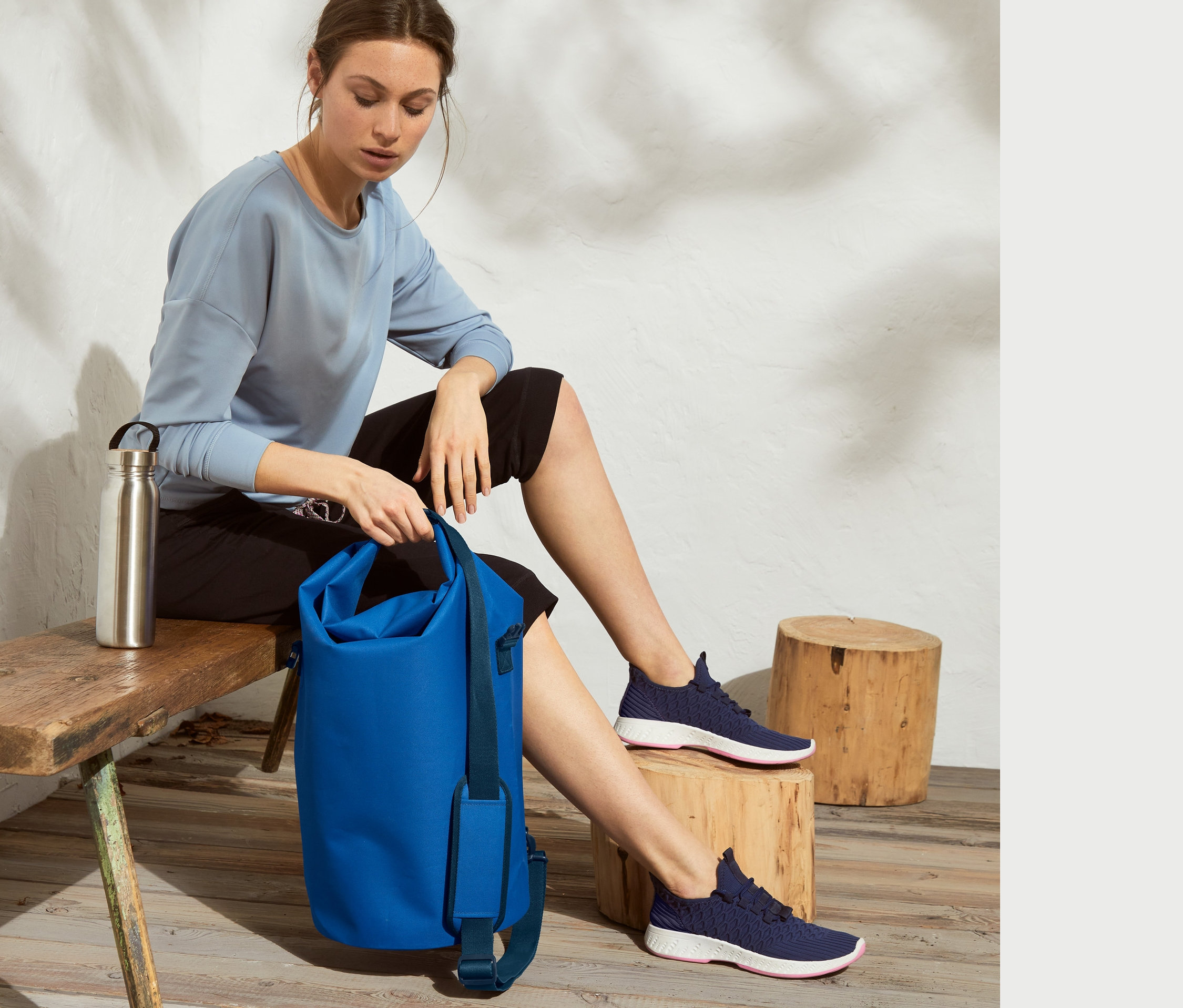 Kadın bankta oturuyor ve mavi Su Geçirmez 25 l Çanta tutuyor.
