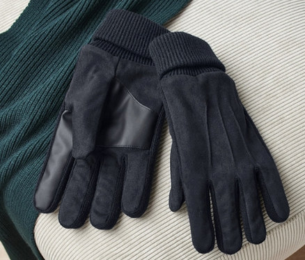 Bej bir taburenin üzerinde bir çift siyah eldiven ve yeşil bir kazak duruyor.