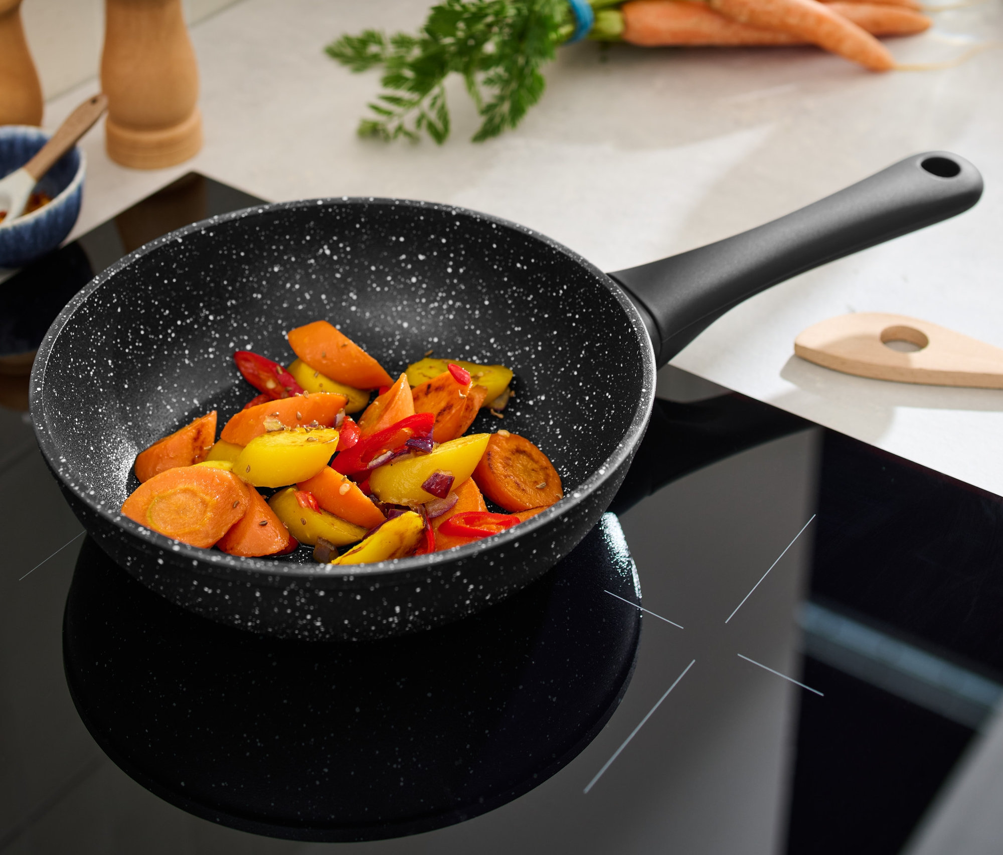 Doğranmış sebzelerle birlikte siyah seramik ocak üzerinde 20 cm çapında taş görünümlü profesyonel tava.