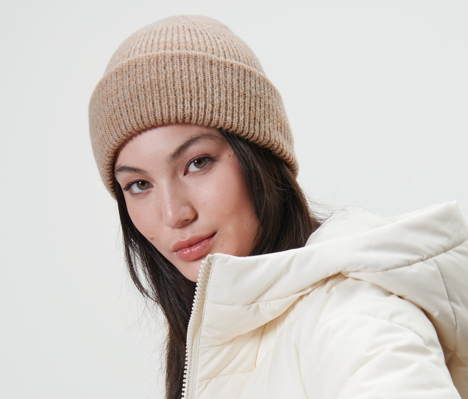 Kadın, ekru rengi örgü bere ve beyaz bir şişme mont giyiyor.