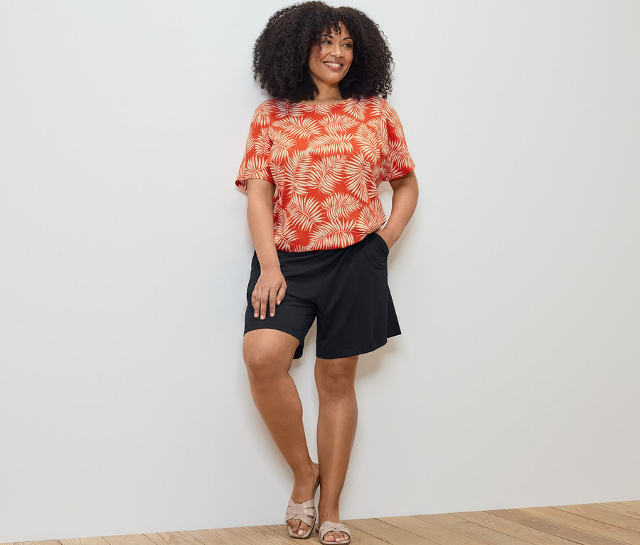 Kadın baskılı bluz ve siyah jarse şortla poz veriyor.